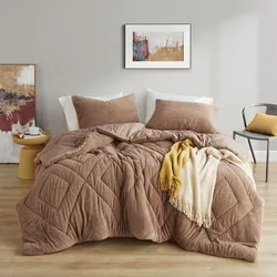 A cozy bedroom setup features a brown quilted comforter, matching pillows, and a draped yellow and cream fringe blanket. Accompanying decor includes abstract wall art, a round yellow side table, and a gray chair with a yellow cushion.
