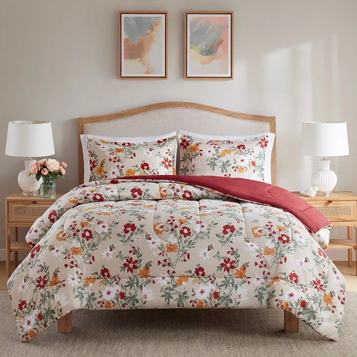 Floral-patterned bedding set on a wooden bed with two matching pillows, accompanied by two white table lamps on side tables, all under two abstract paintings on the wall.