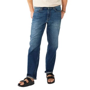 A person wearing straight-cut blue jeans paired with black sandals.