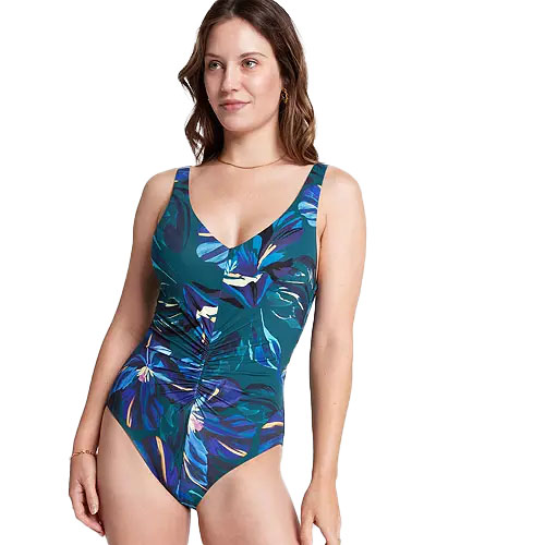 The Calia Ruched Swimsuit features a colorful tropical print with a V-neckline and ruched detailing on the front, designed for a flattering fit.