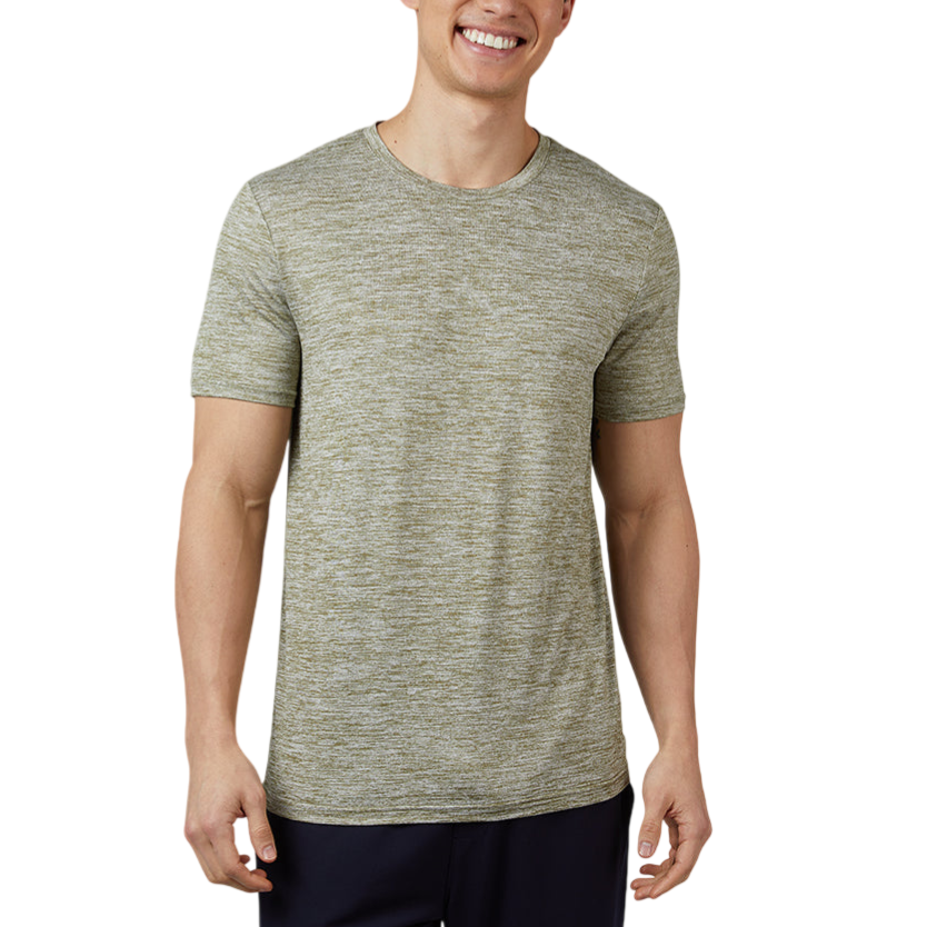 A man is wearing a short-sleeve, heathered green t-shirt with dark pants, standing against a plain gray background.