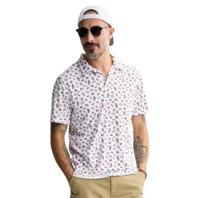 A man wearing a white polo shirt with quirky American-themed graphics, including flags and fireworks, paired with khaki shorts. He's accessorized with sunglasses, a backward white cap, and has tattoos on his left arm.