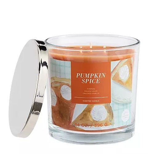 A scented candle in a clear glass jar, labeled \“Pumpkin Spice,\“ featuring images of pumpkin pie.