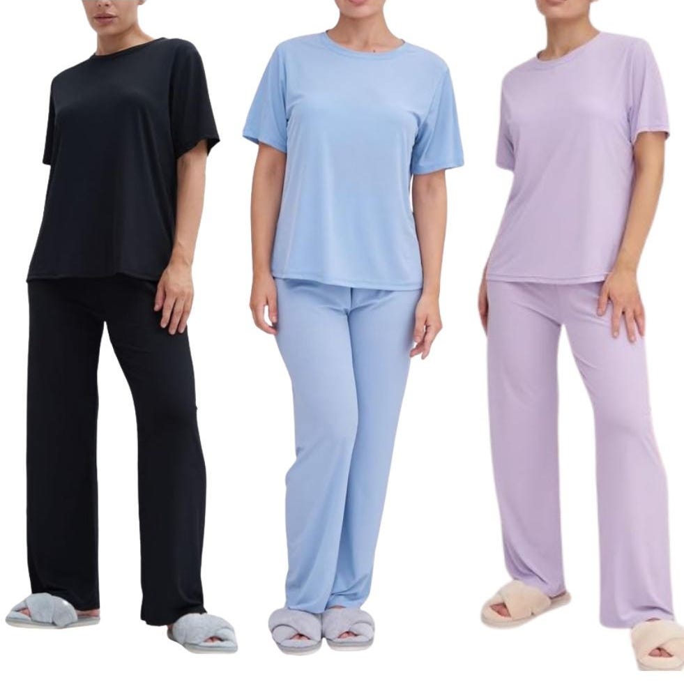 Three women wearing coordinated pajama sets in black, blue, and lavender, each with short-sleeved tops and matching long pants, paired with slippers.