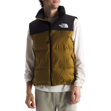 A person wears a brown and black The North Face puffer vest over a white long-sleeve shirt, paired with light-colored pants.