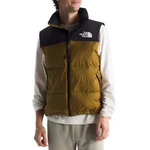A person wears a brown and black The North Face puffer vest over a white long-sleeve shirt, paired with light-colored pants.