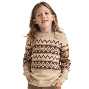 A child wearing a beige and brown geometric patterned sweater, with hands in pockets, surrounded by silver confetti.