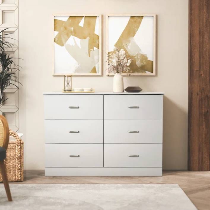 The Tvilum Austin 8 Drawer Double Dresser is a modern, sleek white dresser featuring eight drawers with simple metal handles. It's paired with abstract art and decor, fitting seamlessly into contemporary interiors.
