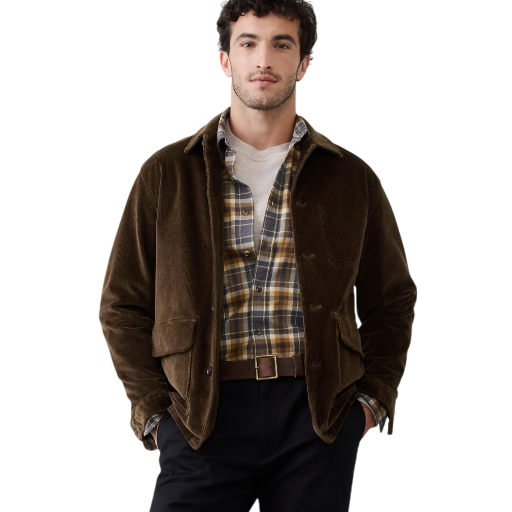 A man wears a brown corduroy jacket over a plaid shirt and white tee, paired with dark pants and a brown belt.