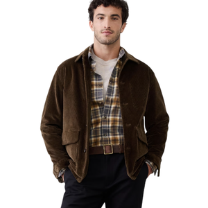 A man wears a brown corduroy jacket over a plaid shirt and white tee, paired with dark pants and a brown belt.