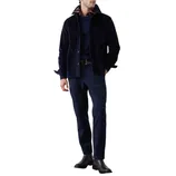 A man wears a navy corduroy jacket over a sweater with a checkered shirt underneath, paired with dark trousers and black leather boots.