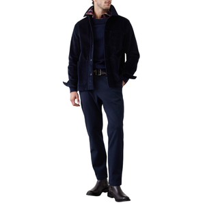 A man wears a navy corduroy jacket over a sweater with a checkered shirt underneath, paired with dark trousers and black leather boots.