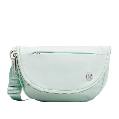 A light mint green lululemon Festival Bag featuring a curved shape, adjustable strap, zippered front pocket, and a simple logo on the front.