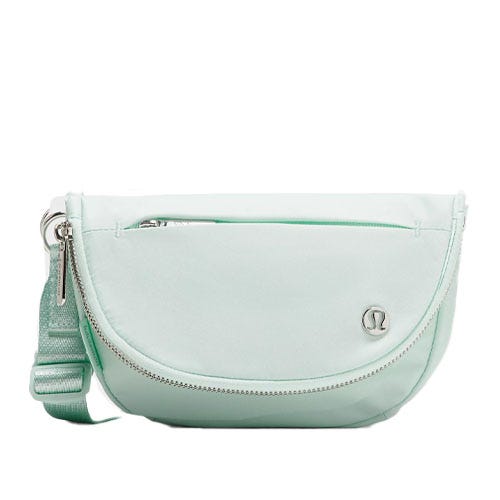 A light mint green lululemon Festival Bag featuring a curved shape, adjustable strap, zippered front pocket, and a simple logo on the front.