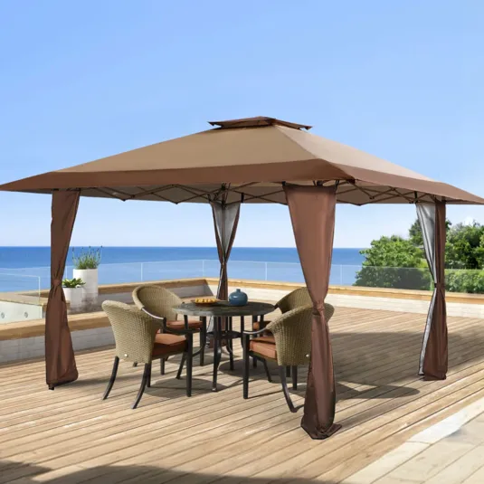 Patio setup featuring a brown fabric gazebo with panel curtains, covering a round black table and four wicker chairs with orange cushions on a wooden deck overlooking the ocean.