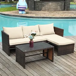 Outdoor wicker patio furniture set with cream cushions, including an L-shaped sofa and a rectangular glass-top coffee table, placed on a wooden deck beside a pool. A decorative vase with flowers sits on the table.