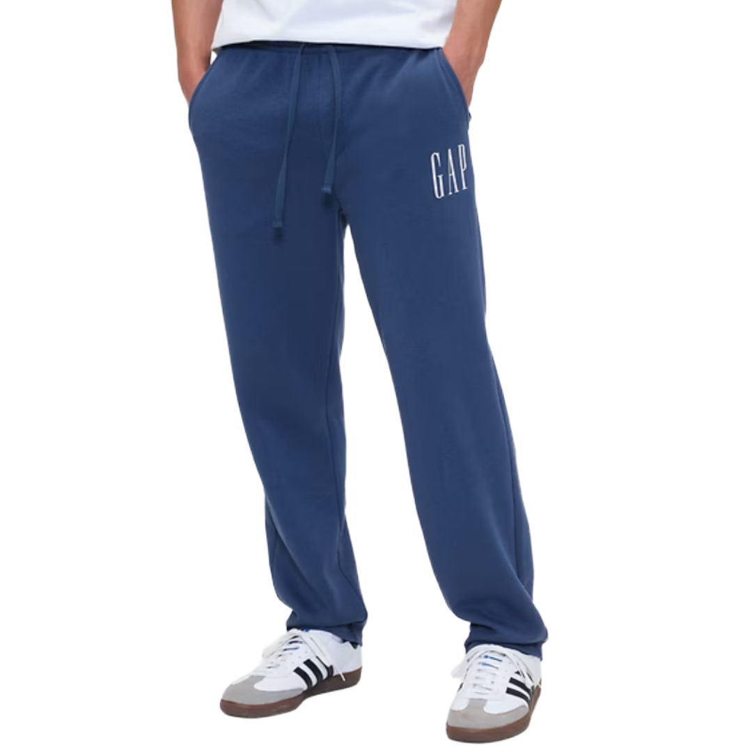 Blue sweatpants with \“GAP\“ logo, elastic waistband, drawstring, and side pockets. Worn with white sneakers featuring black stripes and brown soles.