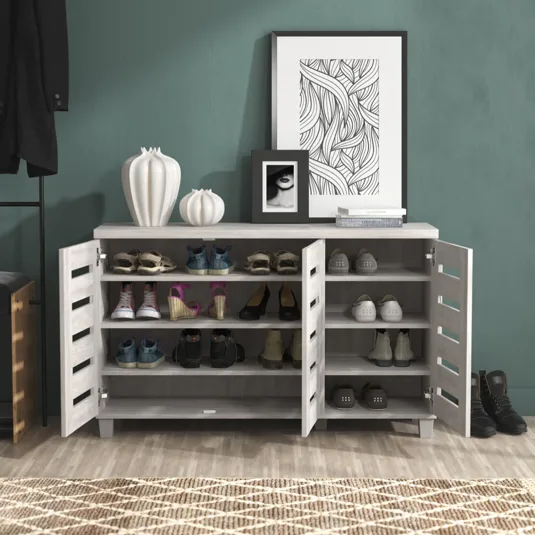 A modern shoe storage cabinet with two doors is shown, featuring multiple shelves holding various shoes. The top is decorated with white vases, framed artwork, and books, set against a textured teal wall.