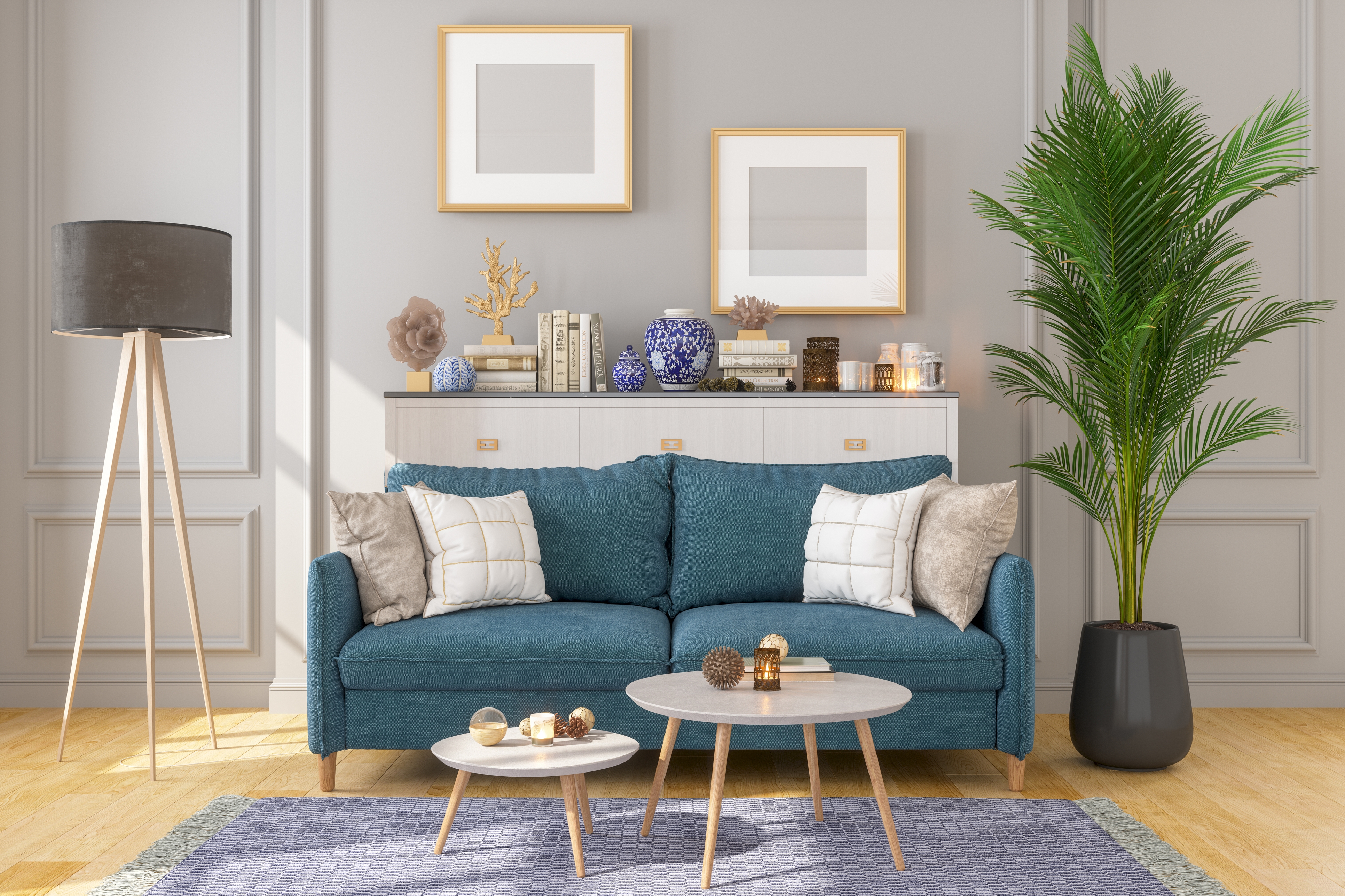 A teal sofa with white and grey pillows, light grey round tables, a tripod floor lamp, and decorative items on a white console with framed artwork above.