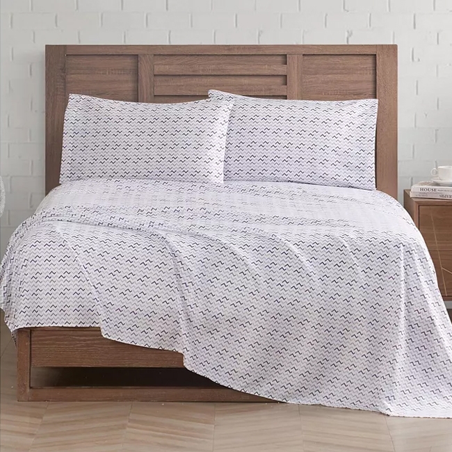 White microfiber sheet set displayed on a wooden bed, featuring a subtle zigzag pattern. The set includes a fitted sheet, flat sheet, and two pillowcases.