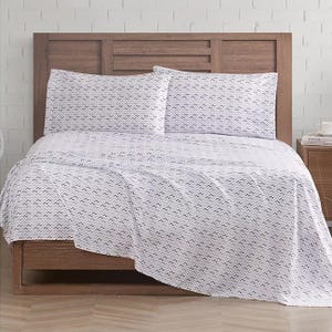 White microfiber sheet set displayed on a wooden bed, featuring a subtle zigzag pattern. The set includes a fitted sheet, flat sheet, and two pillowcases.