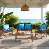Outdoor patio set with wooden chairs and a loveseat featuring blue cushions, a wooden coffee table with a tray, and a woven pendant light overhead, set on a patio with ocean view and surrounded by greenery.