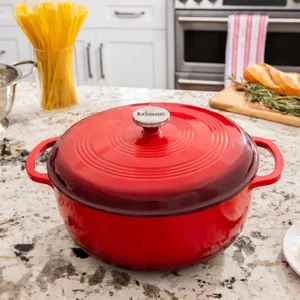 A red enamel-coated cast iron Dutch oven with lid, on a kitchen counter near a container of spaghetti and a cutting board with bread.