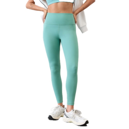 A woman wearing high-waisted, teal-colored leggings styled with a matching sports bra, white sneakers, and a white jacket draped over her shoulders.