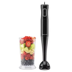 A black hand blender with two-speed settings is next to a clear container filled with assorted fruits, including strawberries, apples, bananas, and berries.