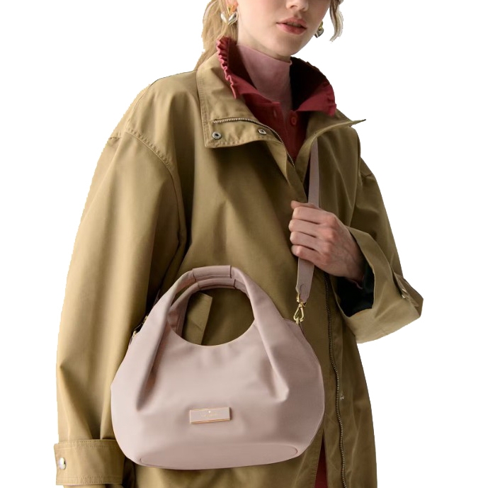 A person in a tan jacket and pink collared shirt holds a light pink handbag with a round handle and shoulder strap.