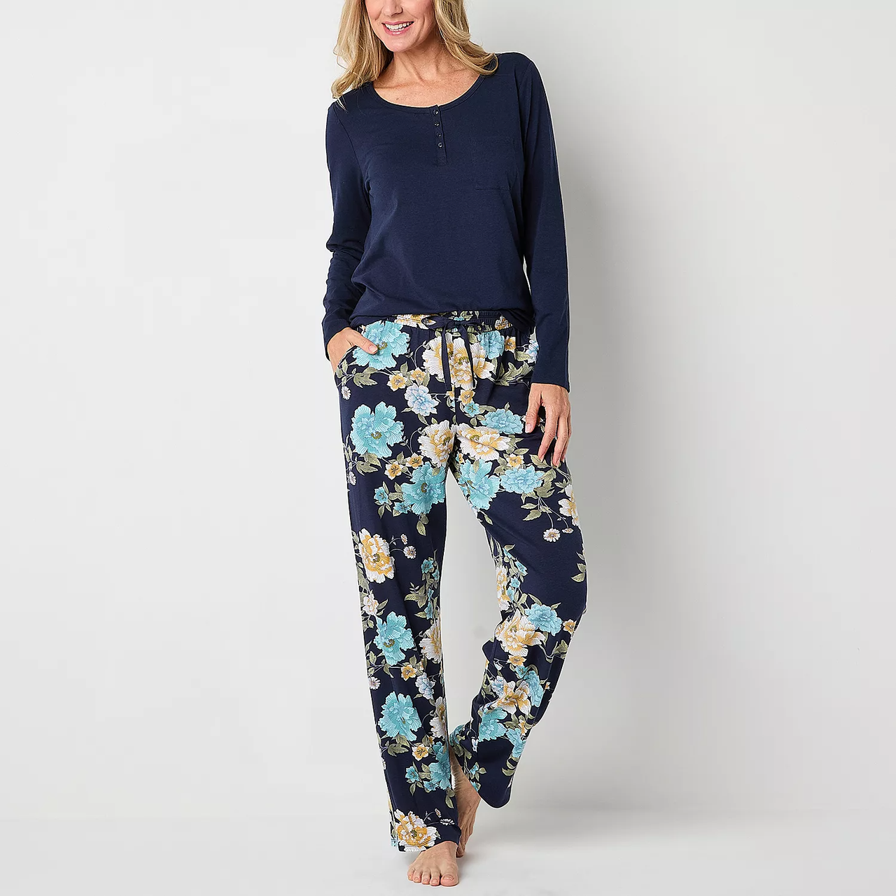 A woman is wearing a navy blue long-sleeve top and floral print pajama pants.
