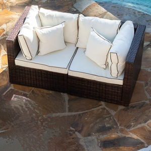 An L-shaped outdoor sectional sofa with white cushions and dark wicker frame, positioned on a stone patio.
