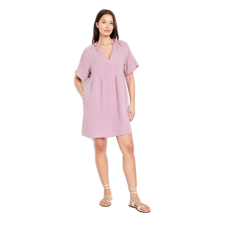 A short-sleeve, light purple mini swing dress with a V-neckline and gathered detailing. Paired with white strappy sandals, it offers a relaxed, casual look.