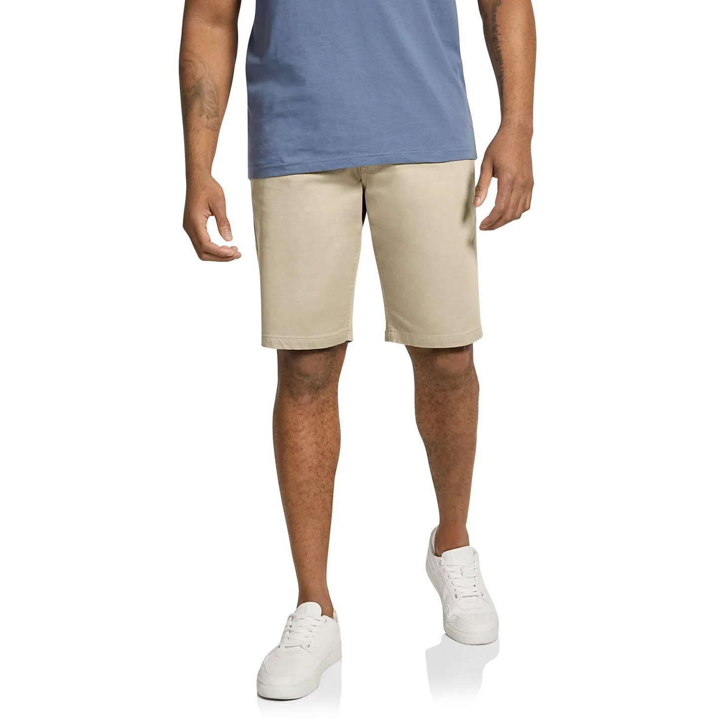 The Johnny Bigg Cameron Knit Shorts are beige, knee-length shorts made from a soft, stretchy knit material, suitable for casual wear. They are paired with a blue shirt and white sneakers.