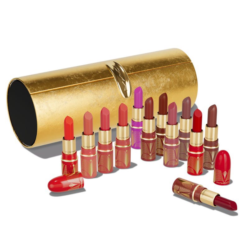 A collection of lipsticks in various shades are displayed in front of a decorative gold-colored cylindrical case. The lipsticks feature ornate designs on their packaging.