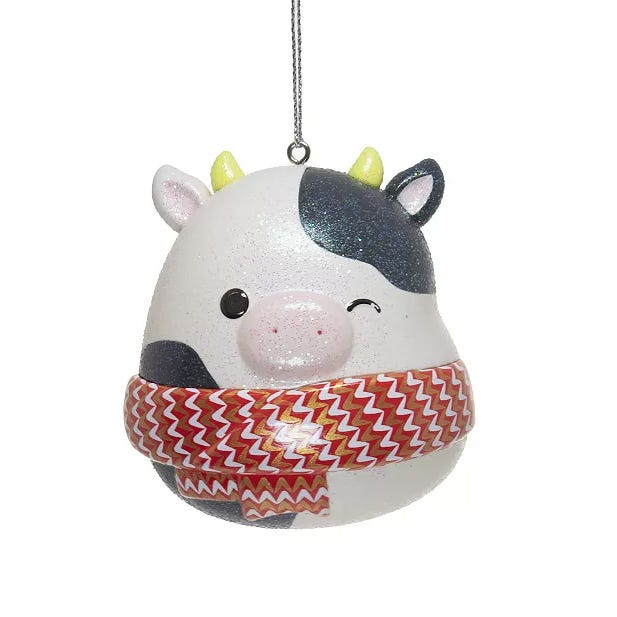 A cute cow-shaped ornament with a winking face, wearing a red and white zigzag-patterned scarf. It features black spots and small horns, ideal for festive decorations.