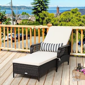 Outdoor steel chaise lounge with dark wicker frame, beige cushion, and a black-and-white striped pillow, set on a wooden deck overlooking a scenic view.