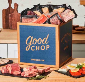 A box labeled \“Good Chop\“ is filled with packaged meats and seafood. Various cuts of meat and fish are displayed on a countertop, including steaks and salmon fillets.