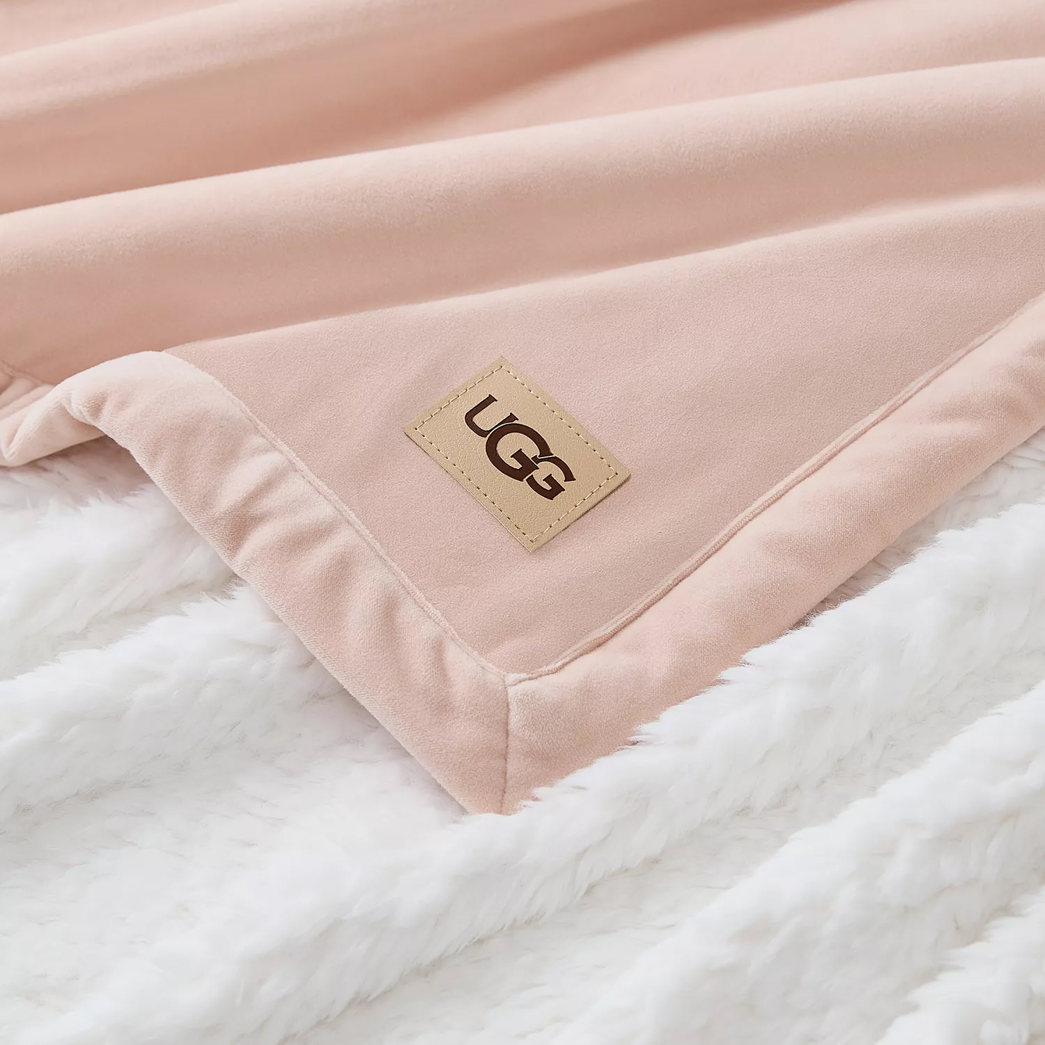 A soft pink UGG blanket with a logo patch on a fluffy white surface.
