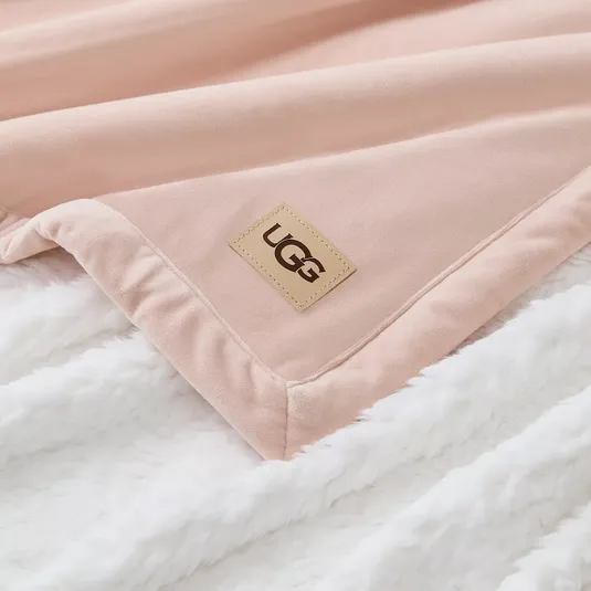 A soft pink UGG blanket with a logo patch on a fluffy white surface.