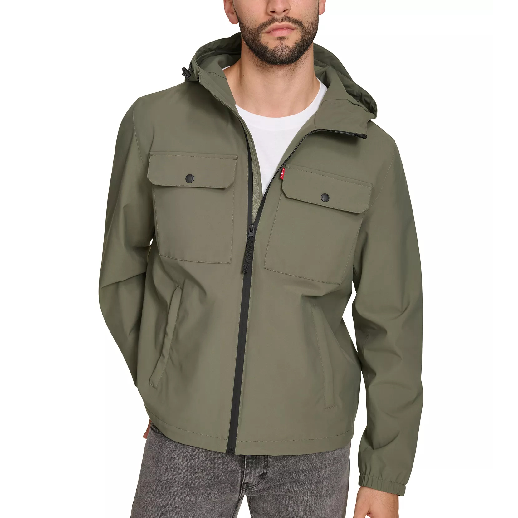 A man is wearing an olive green hooded jacket with front buttoned pockets and a zipper closure, paired with gray jeans.