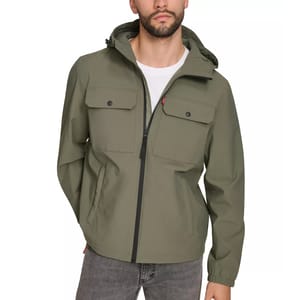 A man is wearing an olive green hooded jacket with front buttoned pockets and a zipper closure, paired with gray jeans.