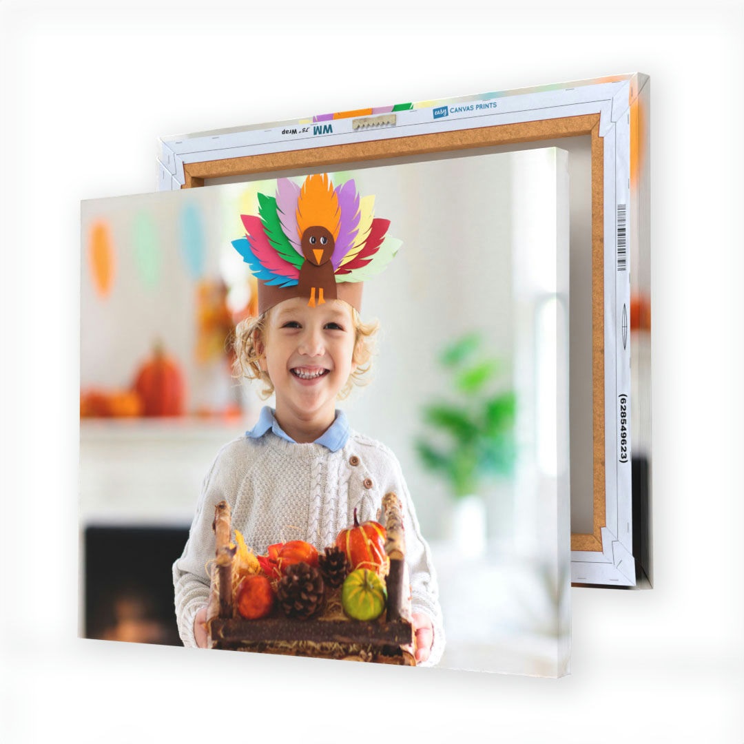 A canvas print features a smiling child wearing a colorful turkey paper crown, holding a crate of small pumpkins and pine cones, with fall-themed decor in the background.