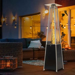 Outdoor patio heater with a modern design, set on a cozy deck with wicker furniture, cushions, string lights, and a warm indoor ambiance visible through glass doors.