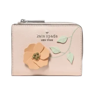 A small, pastel pink wallet with a zip closure, featuring the \“kate spade new york\“ logo and an embossed floral design with a peach flower and green leaves.