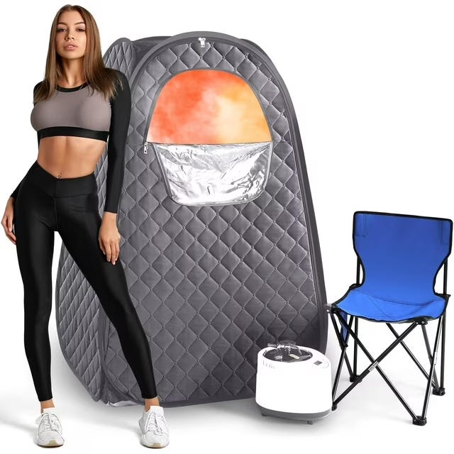 Portable sauna tent with a quilted design, paired with a blue folding chair and steam generator. A person in activewear stands next to it.