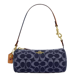 The Coach Outlet Denim Barrel Bag features a denim fabric with the signature Coach pattern, accented by a leather strap and gold-tone hardware. It includes a cherry-themed tag.