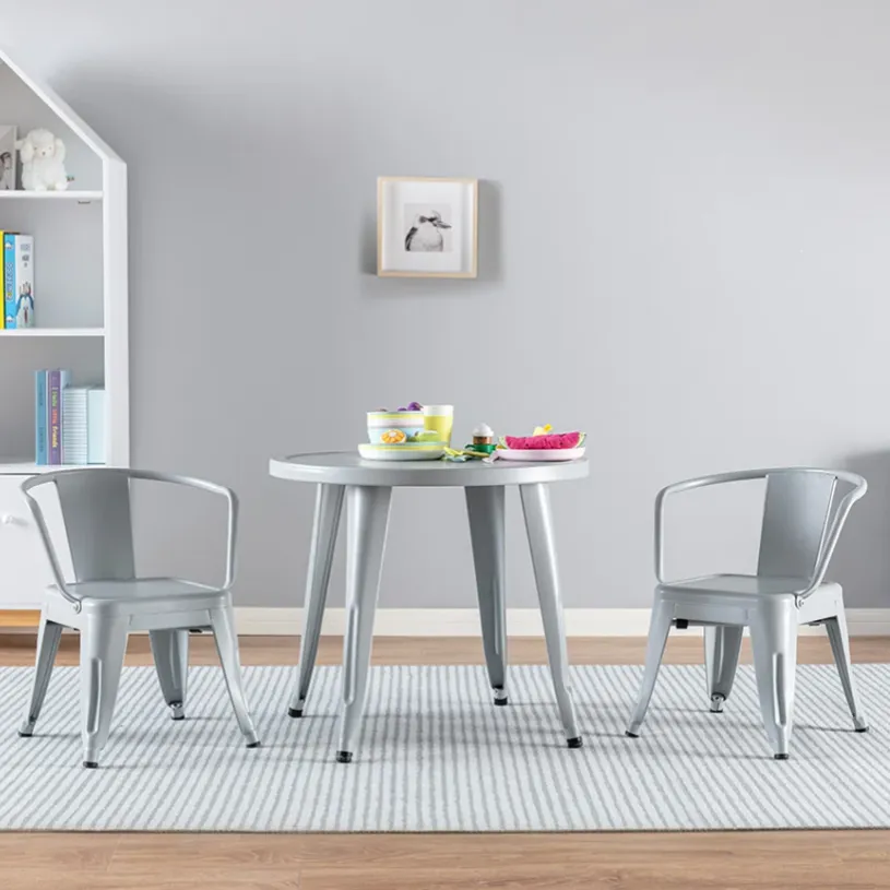 A gray kids' table and chairs set on a striped rug in a playroom with a bookshelf, toys, and books.