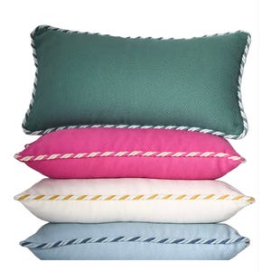Stacked cushions in green, pink, white, and blue with herringbone patterns and twisted rope edges.
