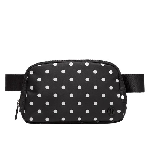 A black belt bag with white polka dots, featuring a front zippered pocket and a sleek adjustable strap.